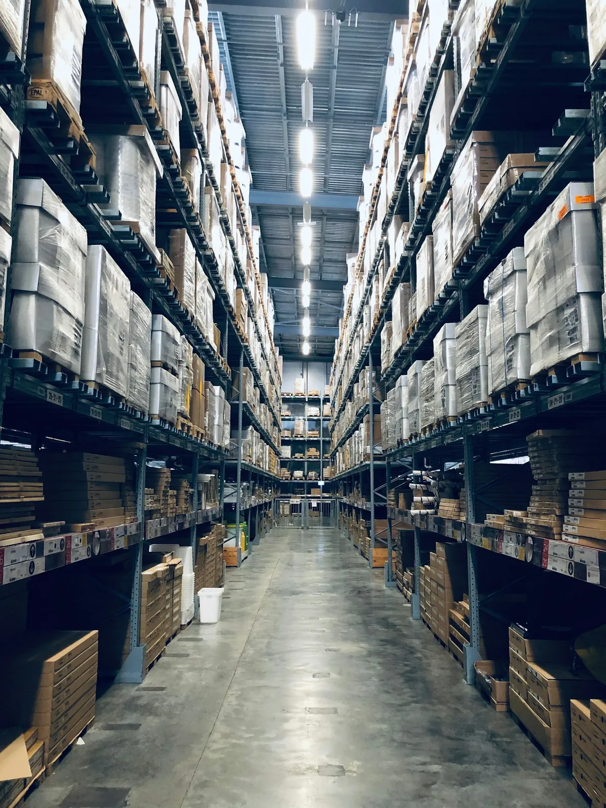 A long warehouse aisle lined with tall pallet racks and cardboard boxes