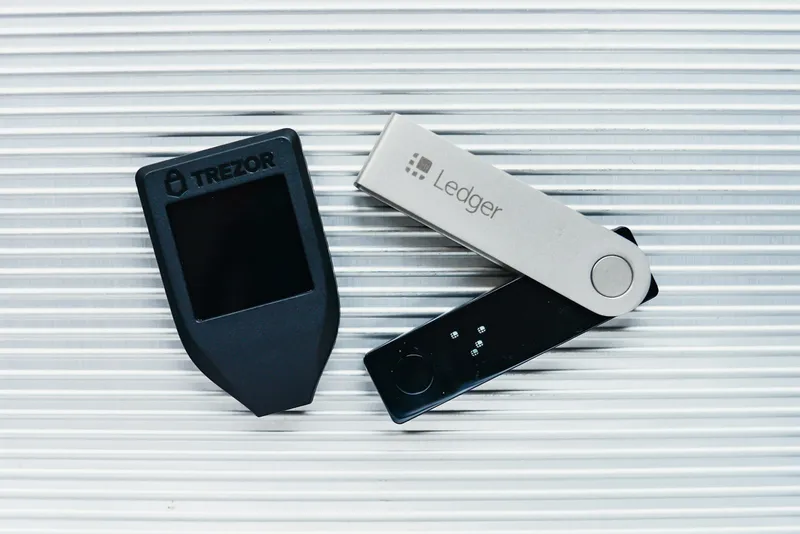 Two hardware cryptocurrency wallets on a desk beside a phone
